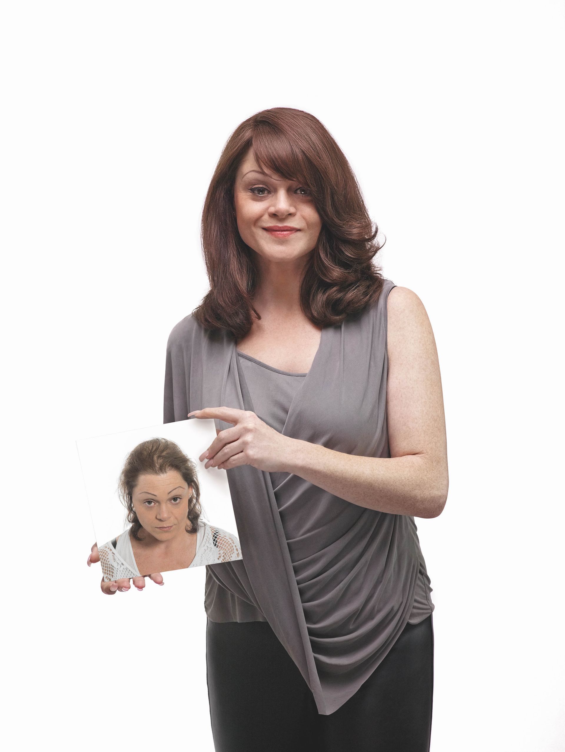 Woman in a gray top holding a small portrait against a white background