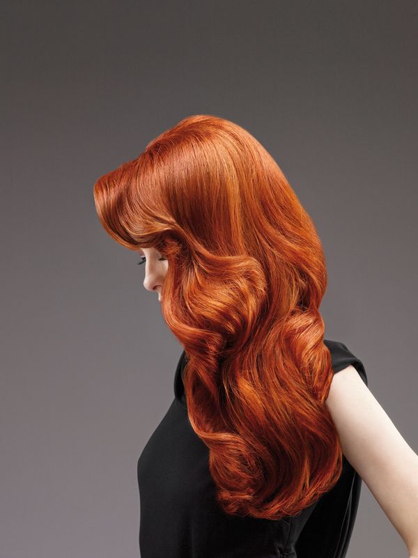 Profile of a woman with long, wavy red hair against a gray background