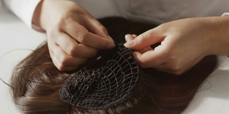 Hands arranging a black mesh hairpiece on brown hair in a close-up