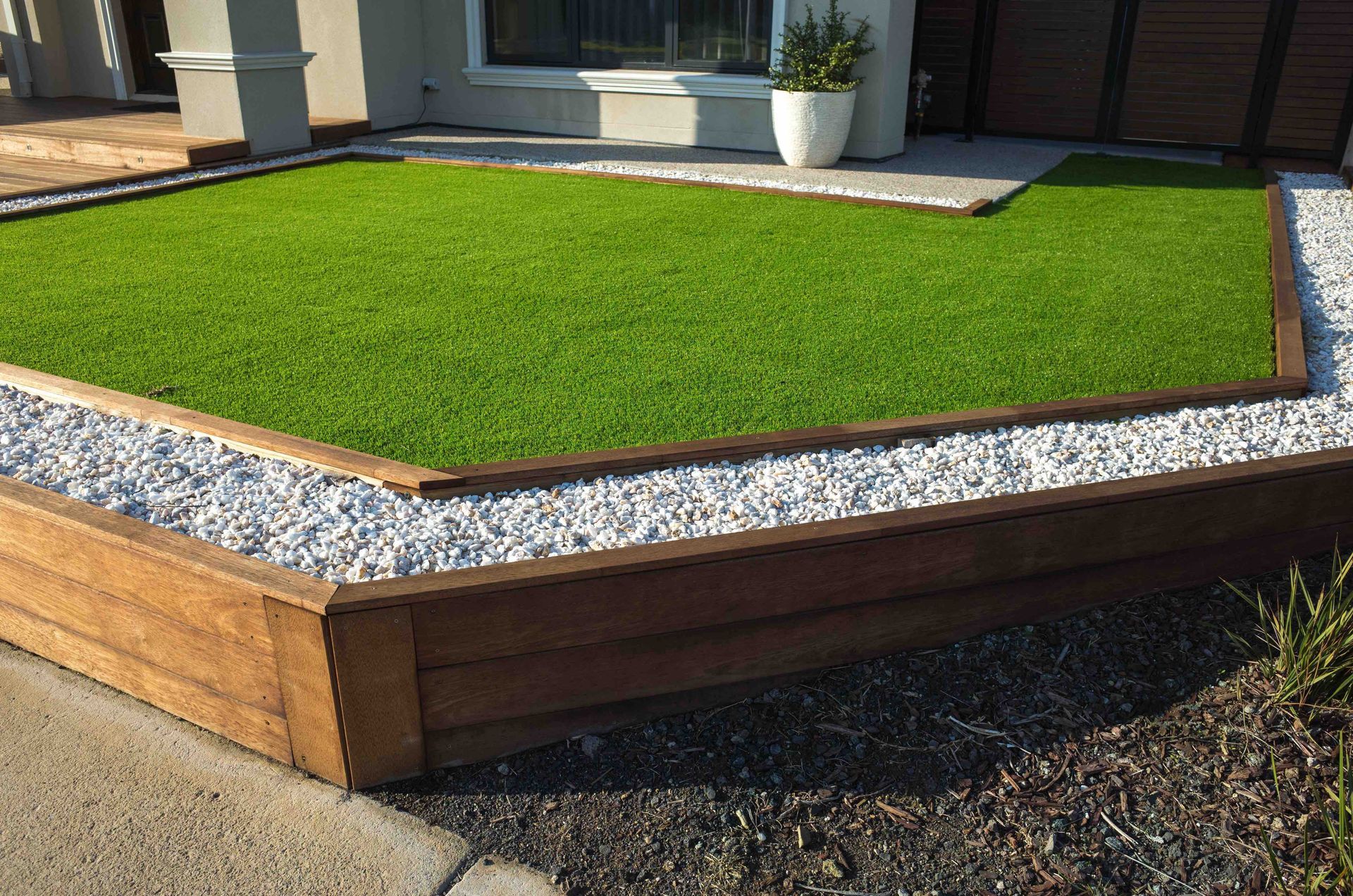 A lawn with a wooden border and gravel in front of a house.