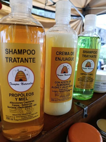 Tres botellas de champú y crema para el cabello sobre un estante de madera, con etiquetas de color ámbar y verde.
