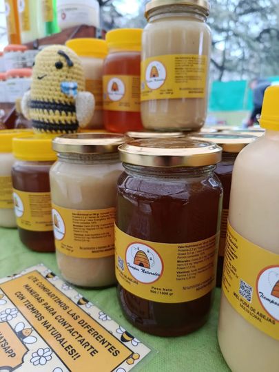 Frascos de miel expuestos, con etiquetas y tapas amarillas, además de una pequeña figurita de abeja al fondo.