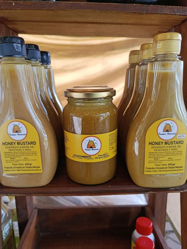 Botellas de miel y un tarro sobre un estante de madera, con etiquetas amarillas y tapas de plástico oscuras y claras.