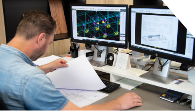 A man is sitting at a desk in front of two computer monitors.