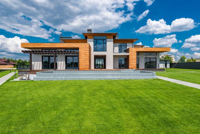 Modern two-story house with wood accents, large windows, and green lawn against a blue sky.