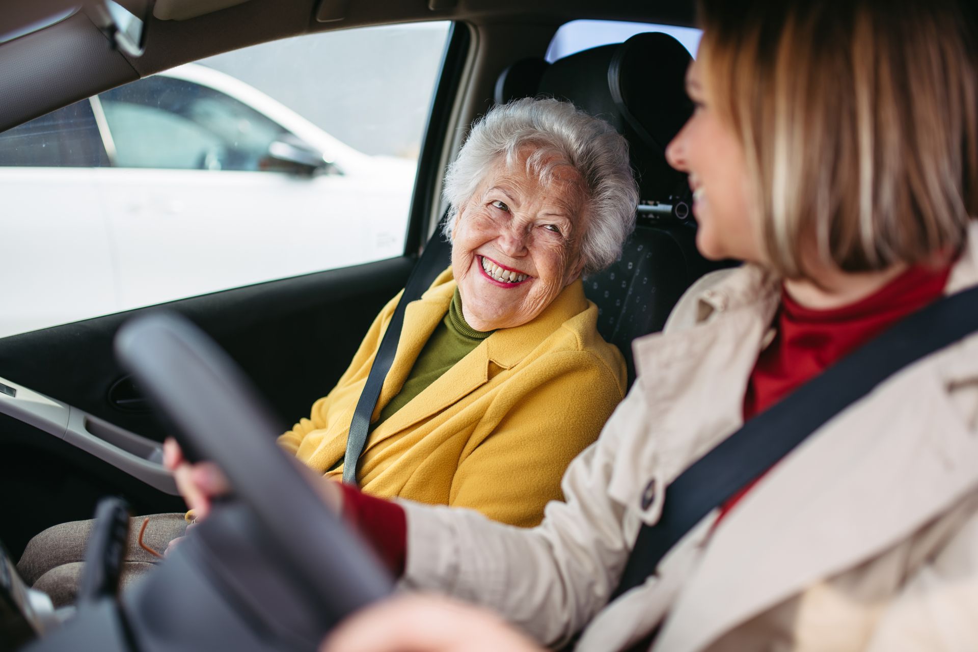 A woman is driving a car with an elderly woman in the back seat.