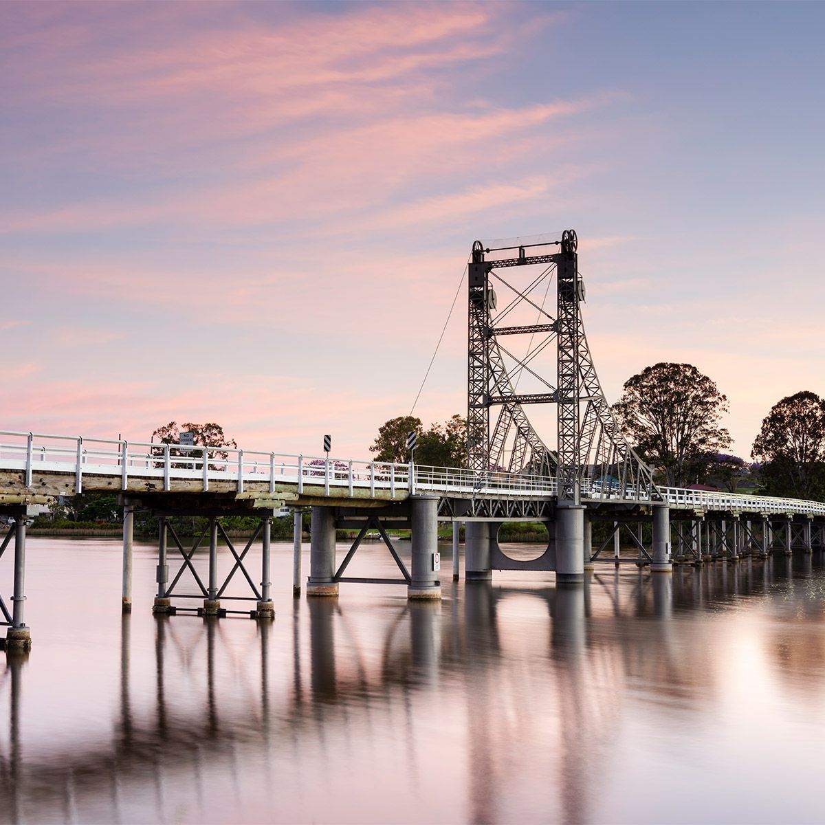 Historic white bridge over calm water at sunset with pink sky and reflections in Maclean