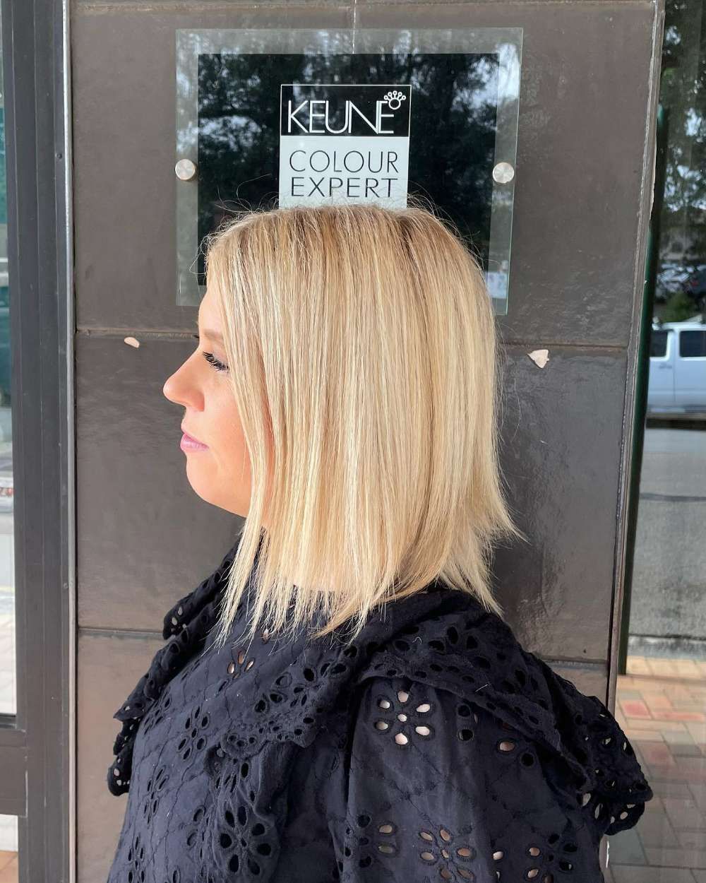 A Woman Stands in Front of a Keune Sign — Innovative Hair Salon in Gosford, NSW