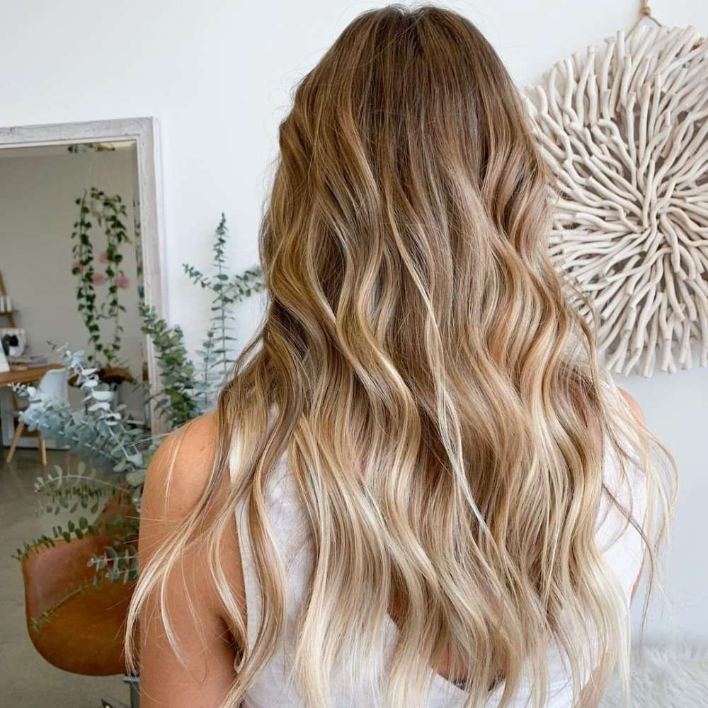 A Woman With Long Blonde Hair is Standing in Front of a Mirror — Innovative Hair Salon in Gosford, NSW