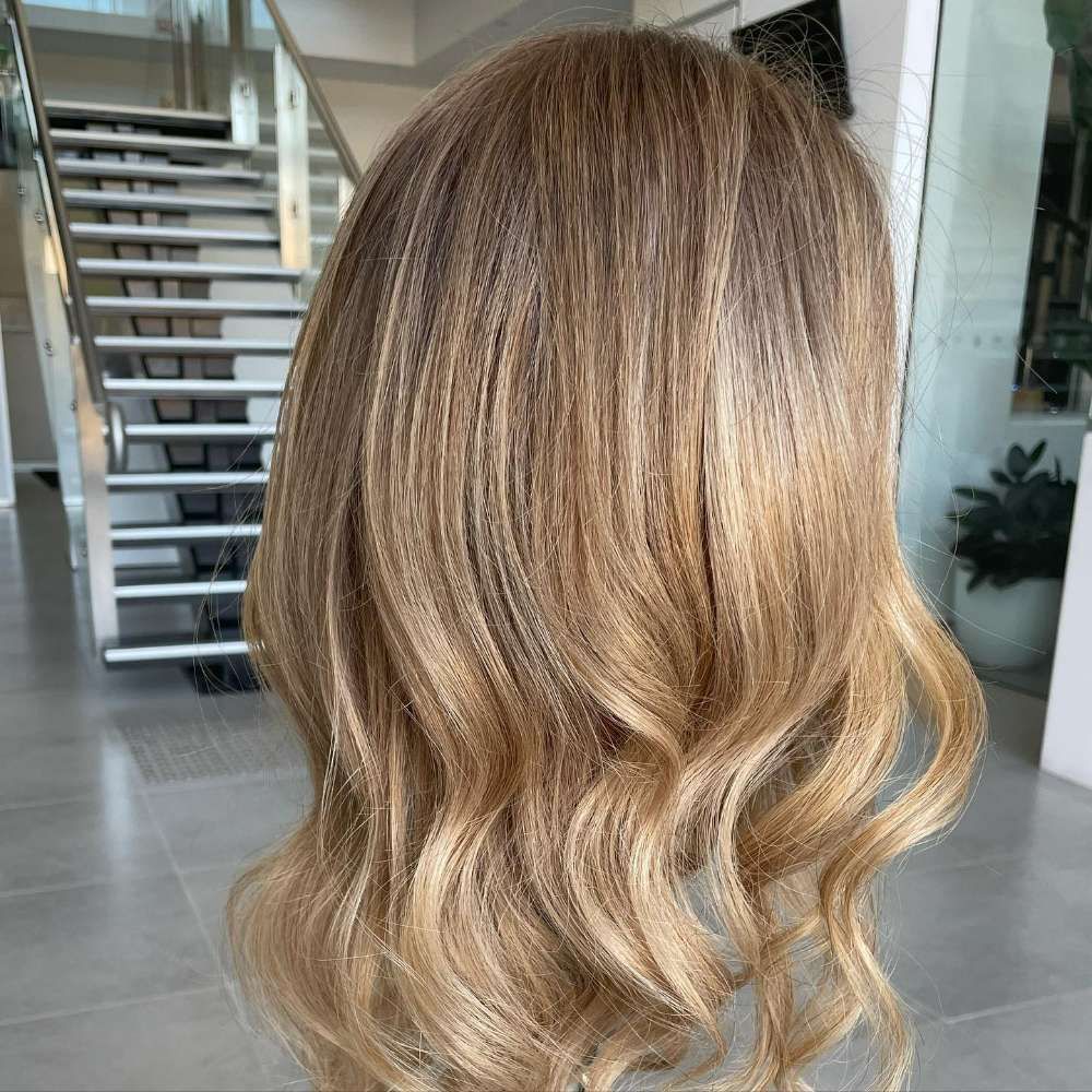 A Woman With Long Blonde Hair is Standing in Front of Stairs — Innovative Hair Salon in Gosford, NSW