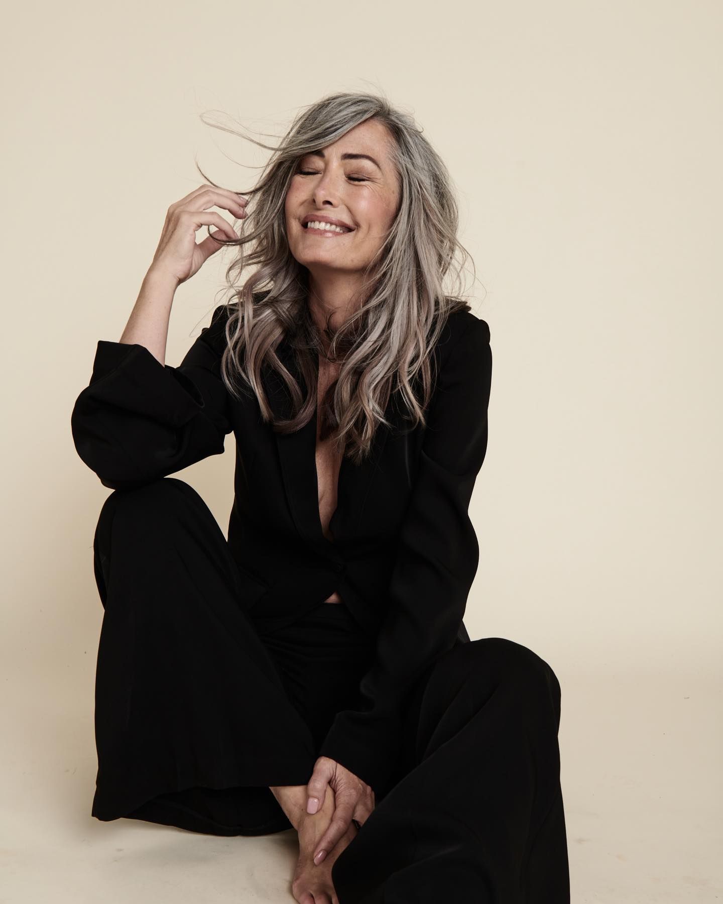 A Woman With Gray Hair is Sitting on the Floor and Smiling — Innovative Hair Salon in Gosford, NSW