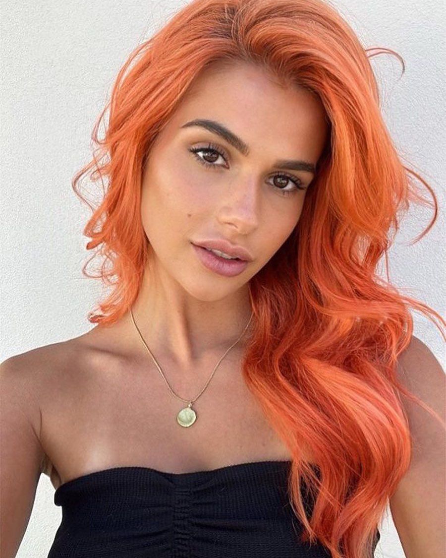 A Woman With Bright Orange Hair is Wearing a Black Top and a Gold Necklace — Innovative Hair Salon in Gosford, NSW