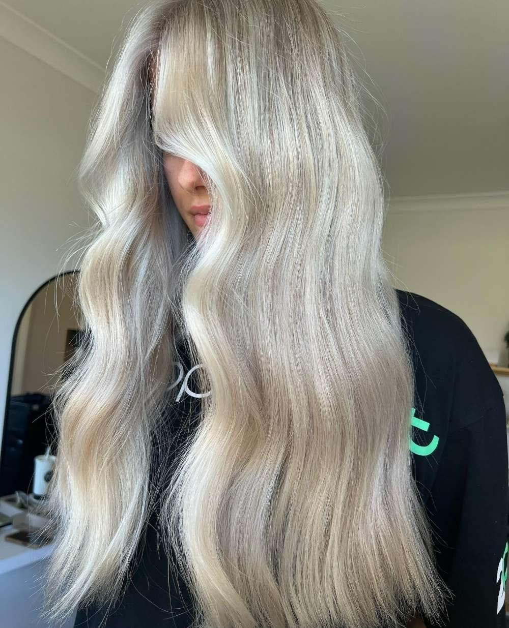 A Woman With Long Blonde Hair is Wearing a Black Shirt With the Logo on It — Innovative Hair Salon in Gosford, NSW