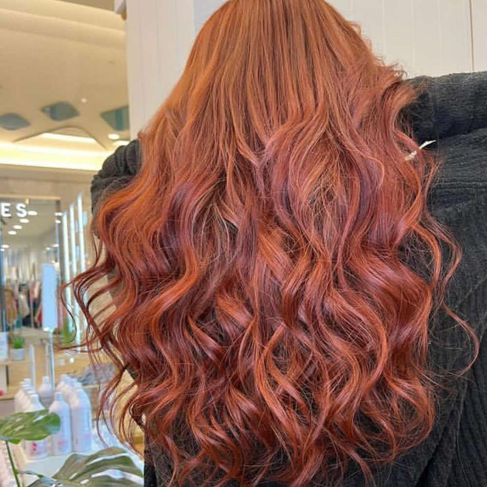 A Woman With Long Red Hair is Standing in Front of a Mirror in a Salon — Innovative Hair Salon in Gosford, NSW