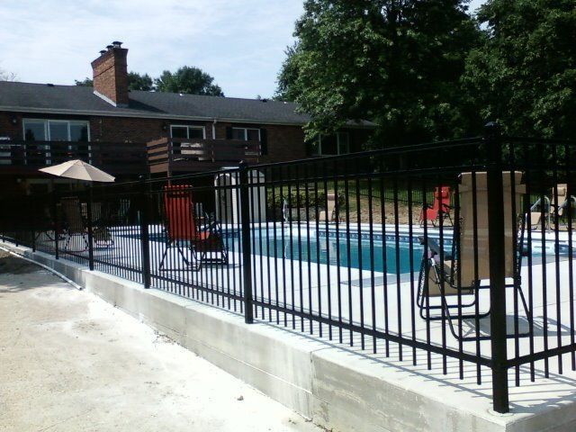 A black fence surrounds a swimming pool in front of a house