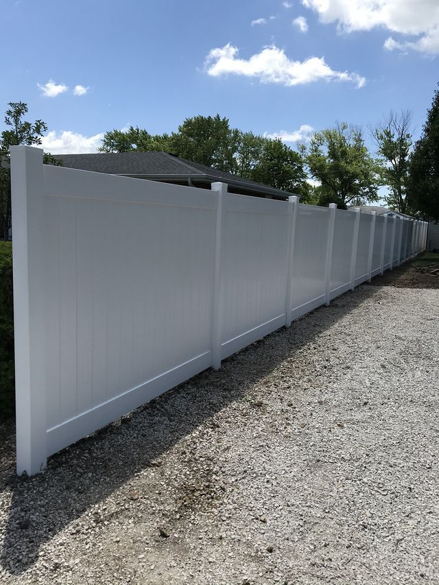A white fence is sitting on top of a gravel driveway next to a house.