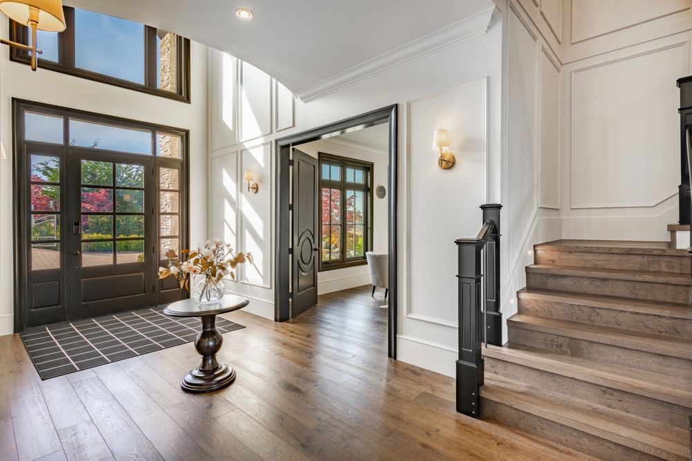 Elegant home entryway with wood floors, staircase, and open doorway to exterior.