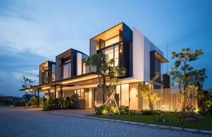 Modern multi-story homes with square geometric design, lit up at dusk.
