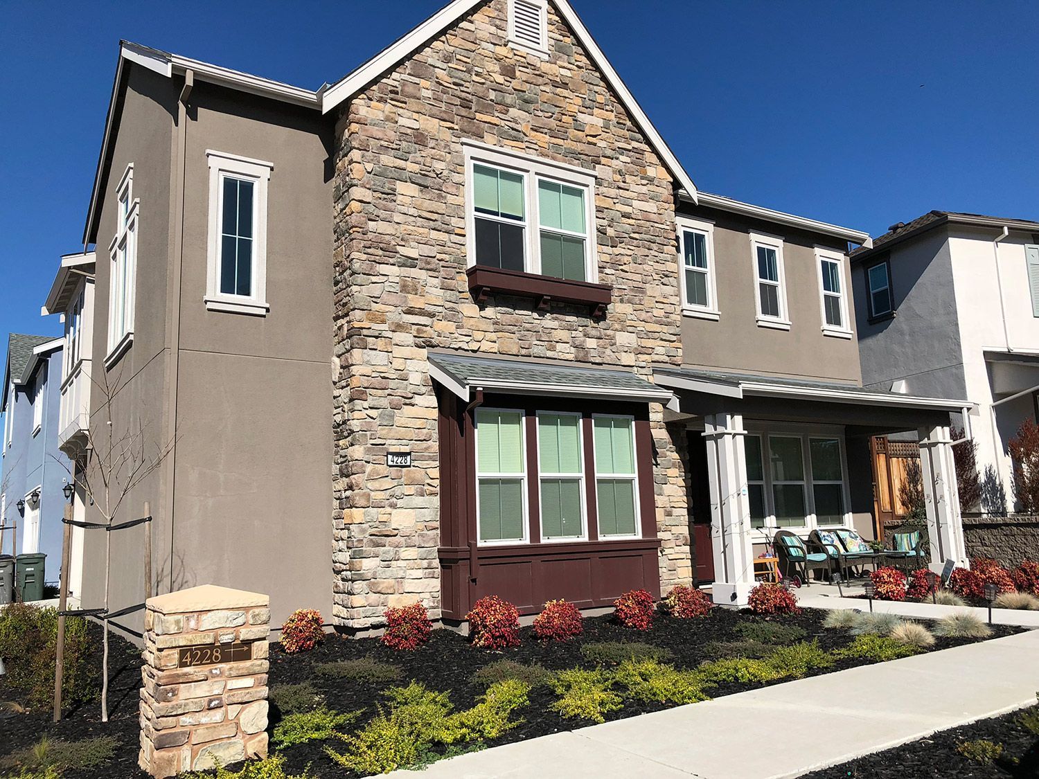 Two-story house with stone facade, stucco walls, and a porch, set against a blue sky.