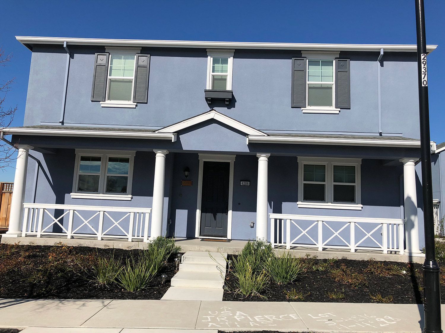 Blue two-story house with white trim, porch, and shutters. Black door, blue siding, and small plants in front.