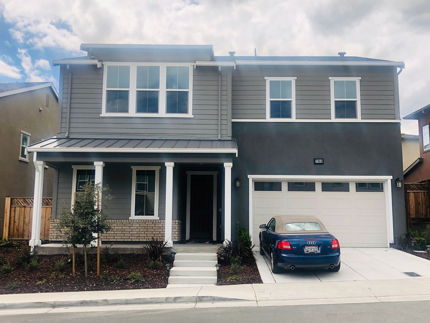 Two-story house with gray and stucco facade, a garage, and a car in the driveway.