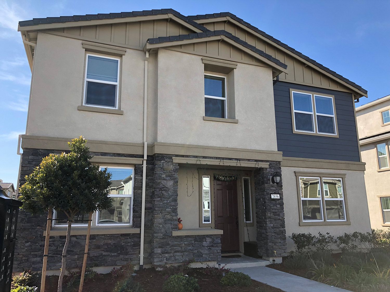 Two-story house with tan, blue, and stone facade; windows reflect the sky.