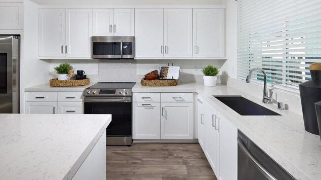 Modern white kitchen with stainless steel appliances, gray floor, and large island in bright natural light