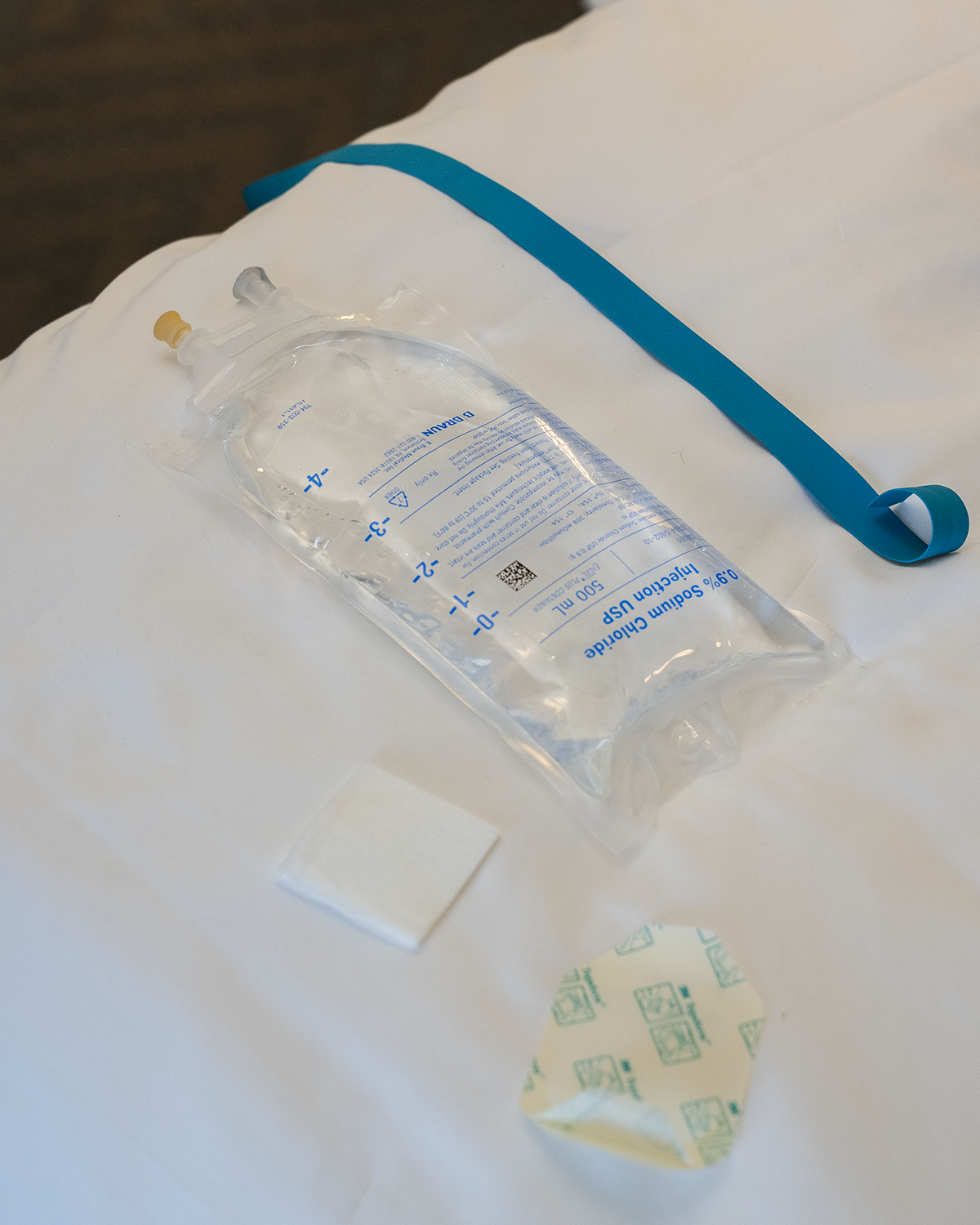 Woman lounging on a white sofa in a bright room, smiling beside an IV stand.