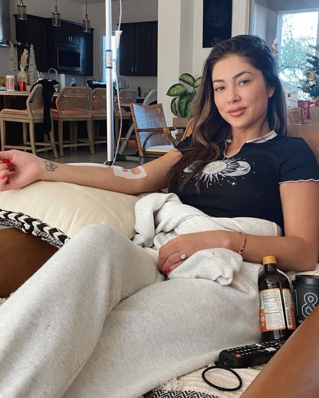 Woman reclining on a couch in a living room, holding a white dog and a bottle nearby.