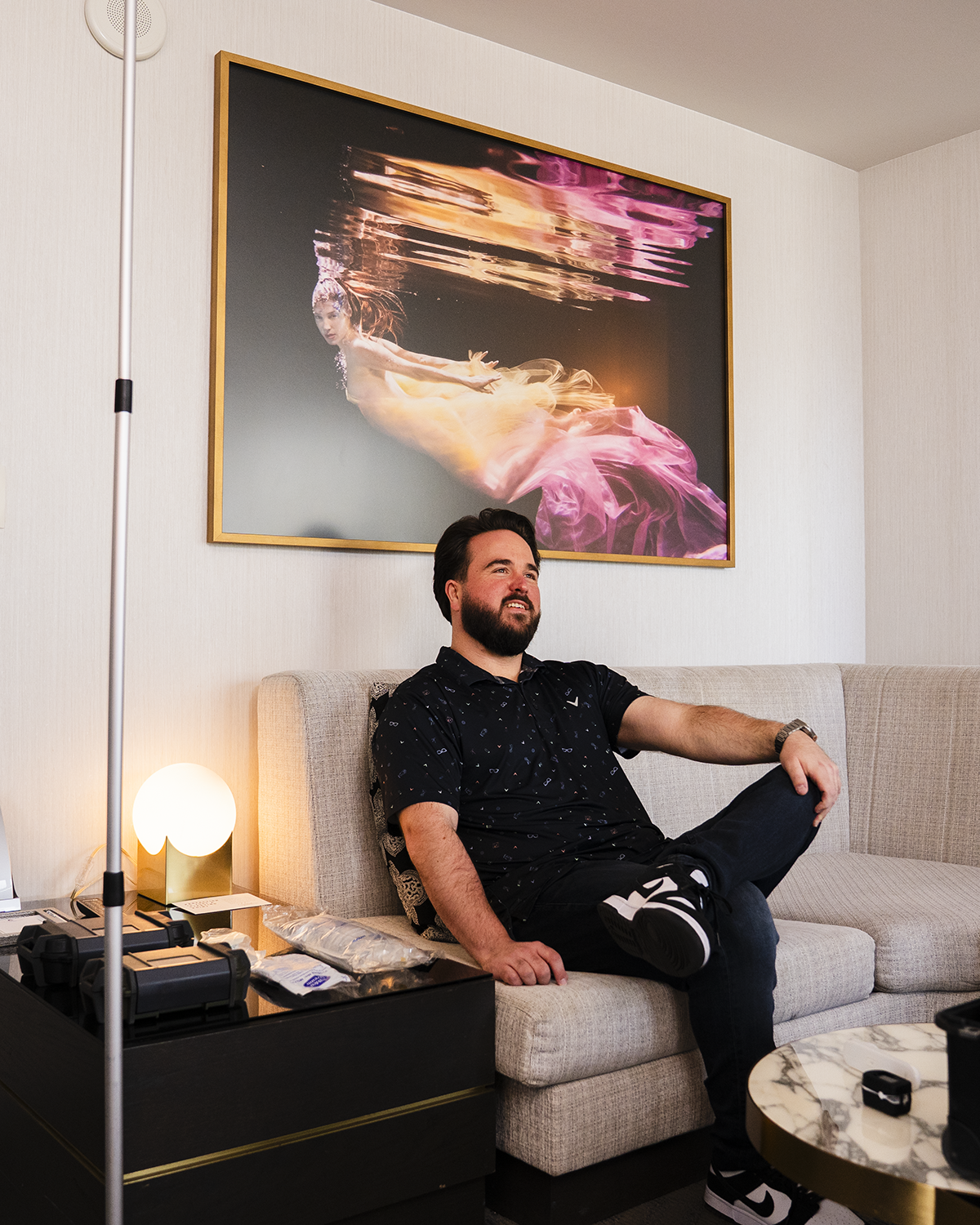 Man relaxing on a sofa in a living room, beneath a colorful framed portrait.