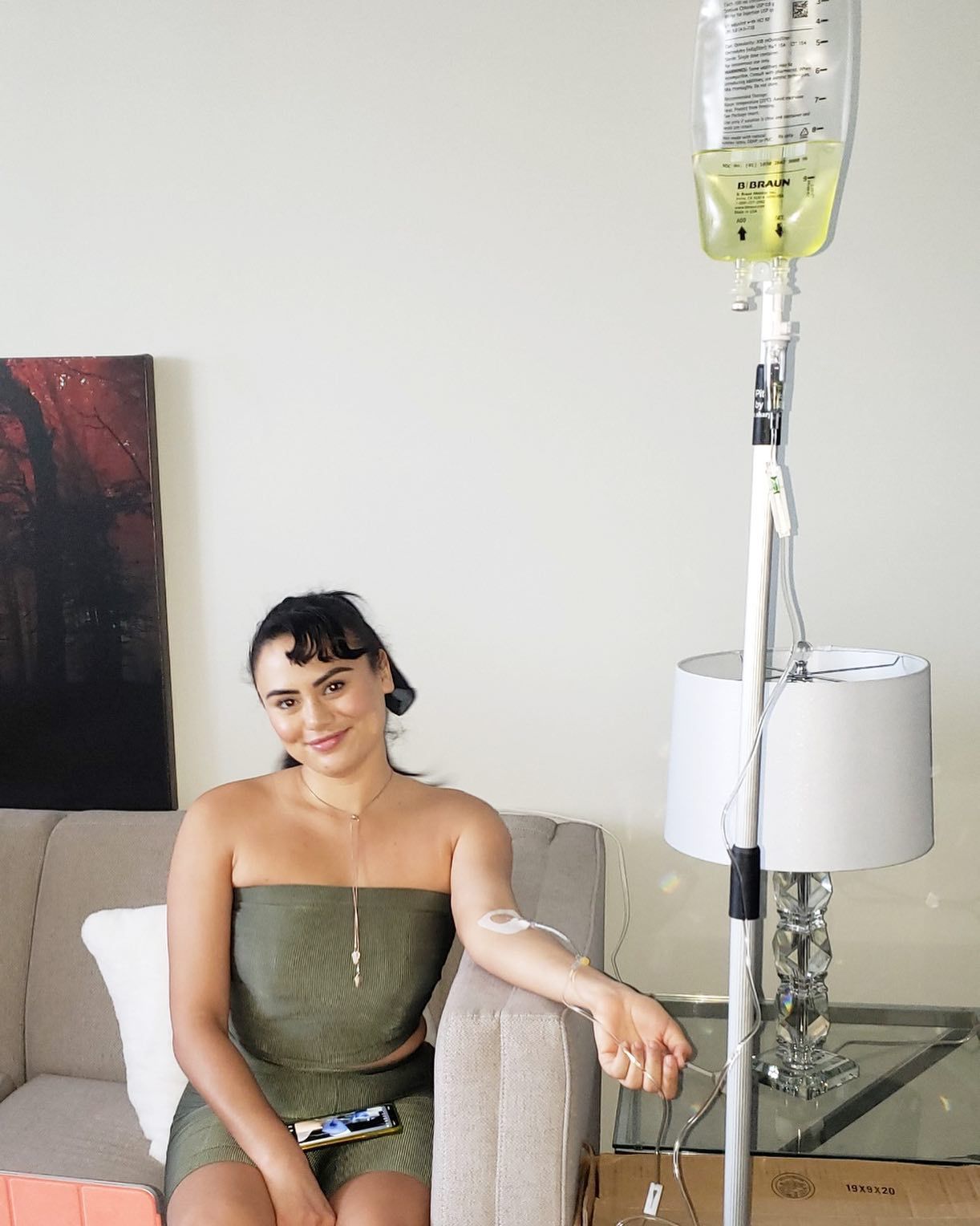 Woman sitting on a couch with an IV drip beside her in a living room setting