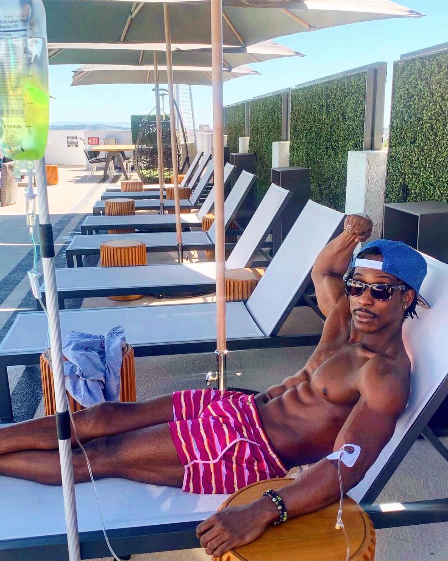 Man reclining on a lounge chair by a pool, wearing sunglasses and pink striped shorts.