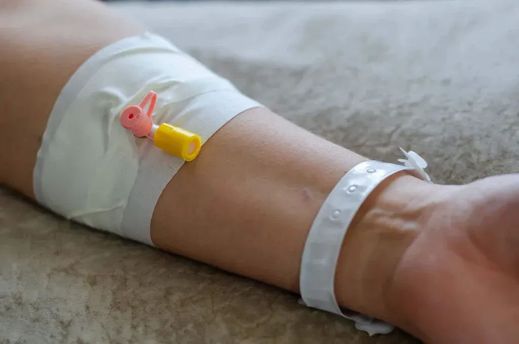 Arm with IV catheter and medical tape resting on a bed
