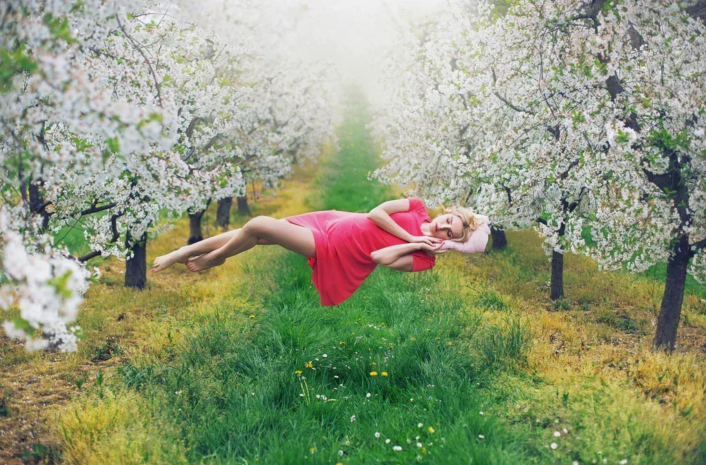 Woman in a pink dress floating horizontally above grass in a blooming orchard