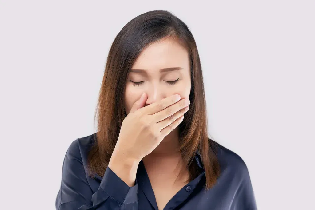 Woman covering her mouth with her hand against a plain light background