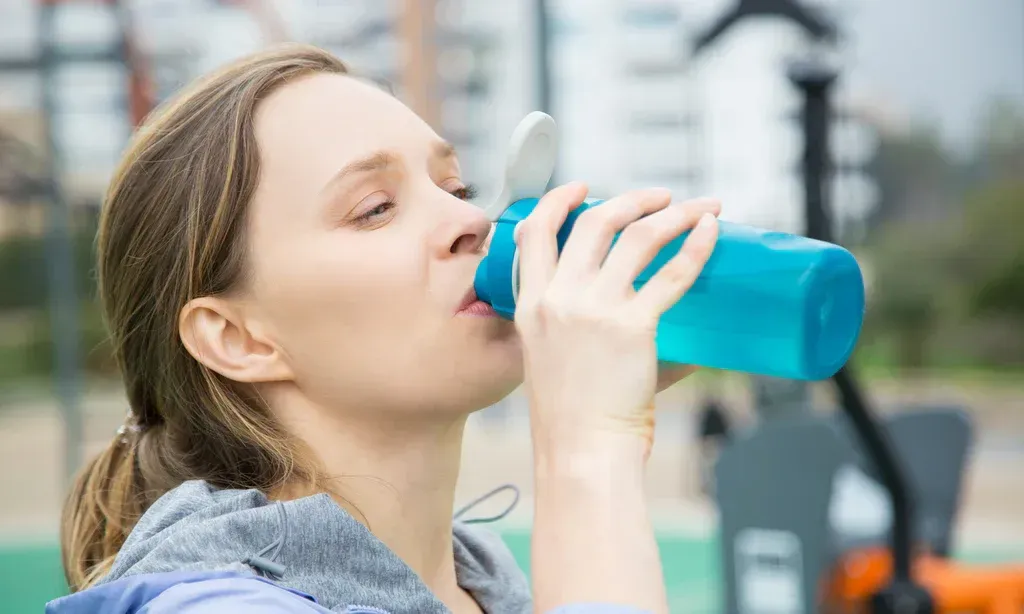 Person drinking from a blue water bottle outdoors