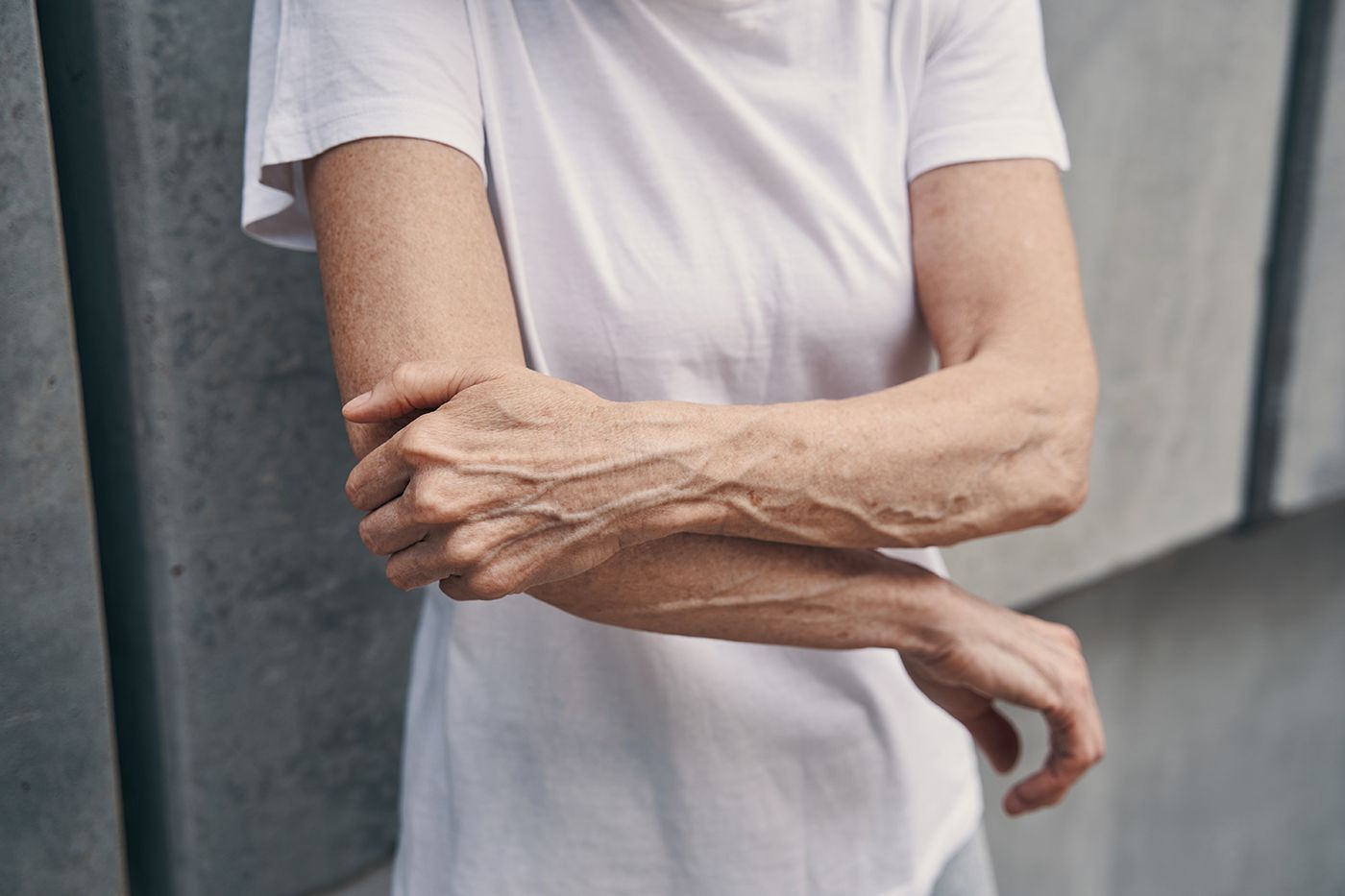 Person in a white T-shirt rubbing their forearm against a gray wall