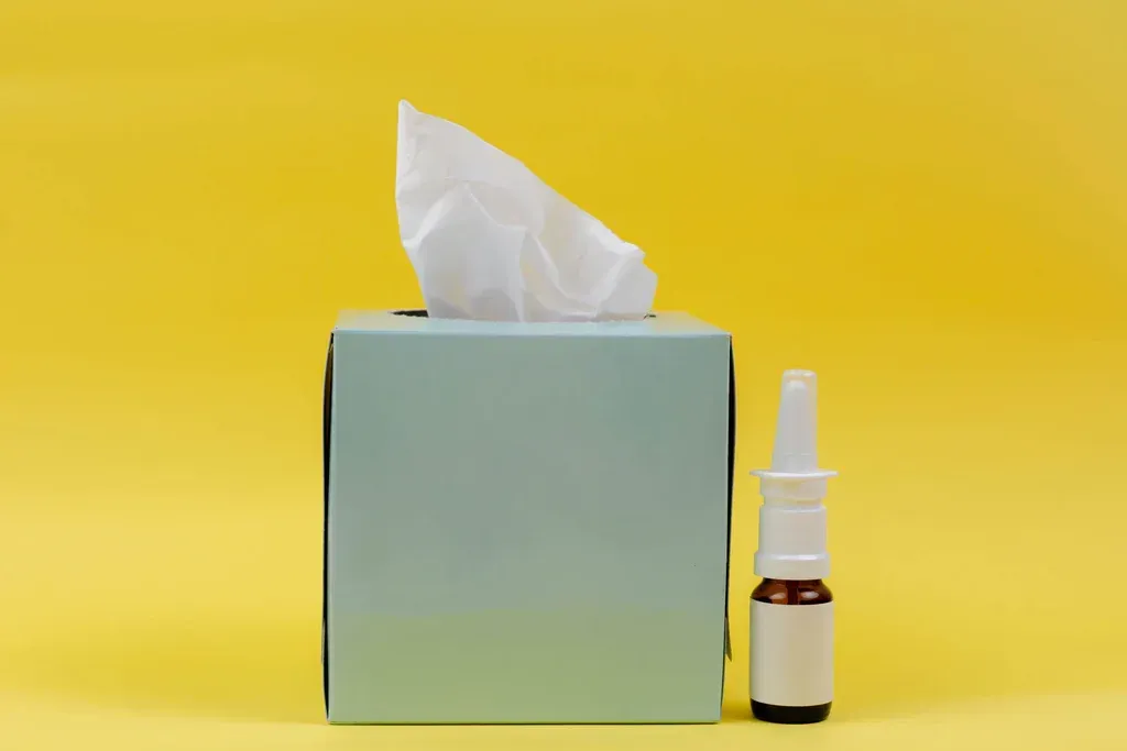 Tissue box with a white tissue and small nasal spray bottle on a yellow background