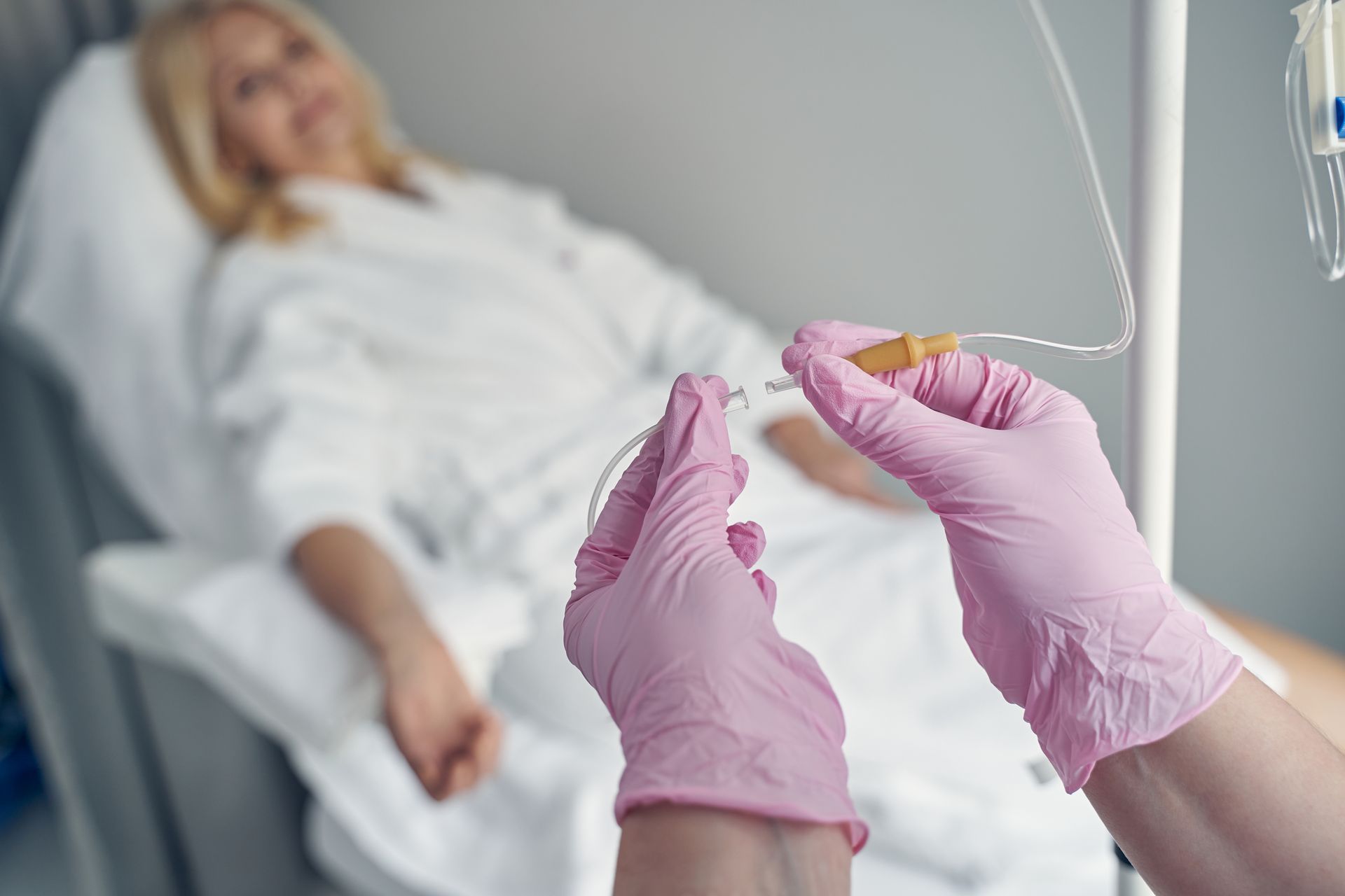 Gloved hands holding a swab in front of a patient lying in a hospital bed