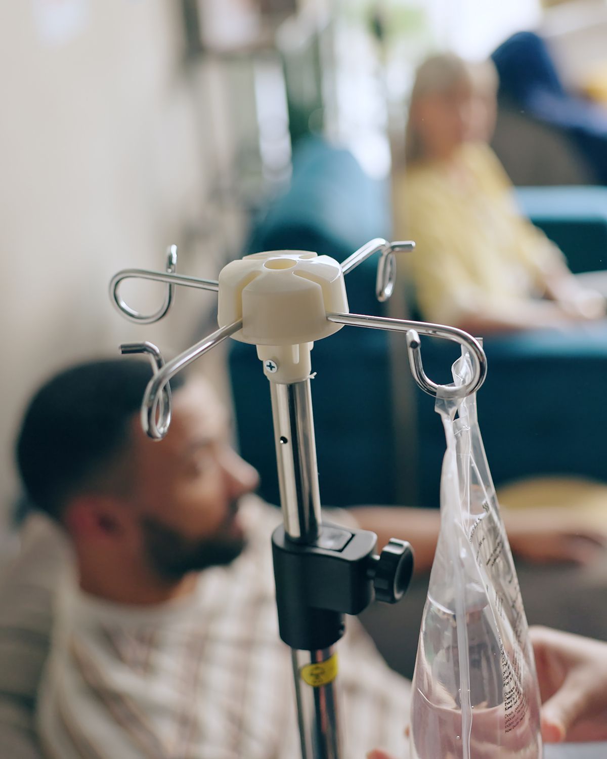 Woman lounging on a white sofa in a bright room, smiling beside an IV stand.