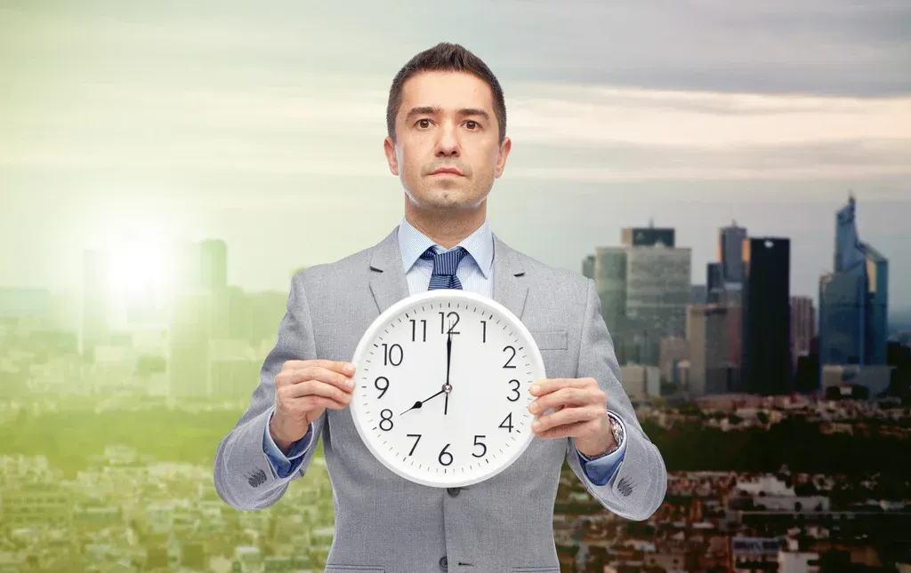 Businessman holding a clock in front of a city skyline and sunrise gradient background