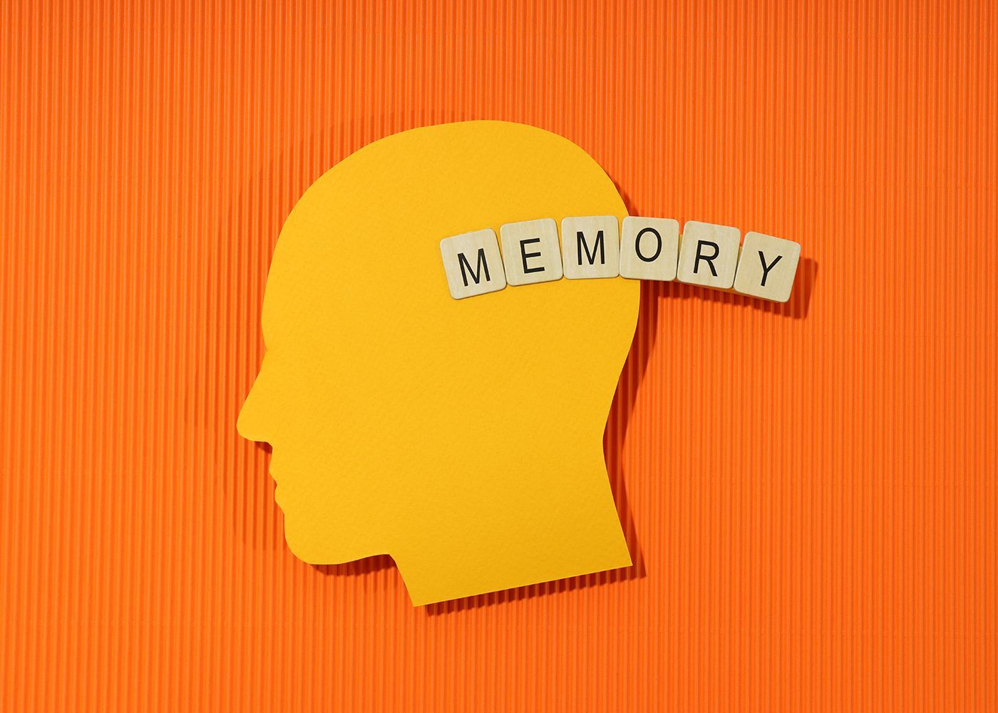 Yellow head silhouette with “MEMORY” letter tiles on an orange background