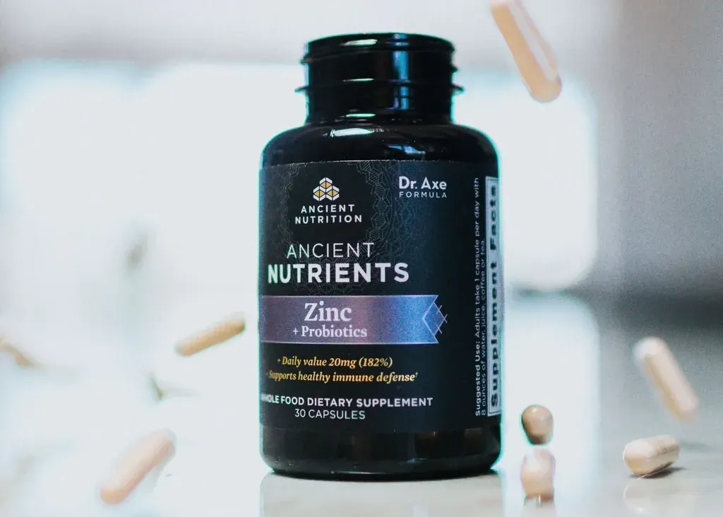 Black bottle of Ancient Nutrition Zinc + B vitamins with pills scattered around it on a white background