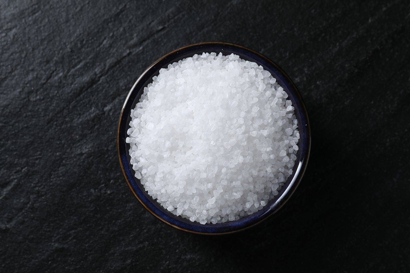 Small bowl of coarse white salt on a dark stone surface