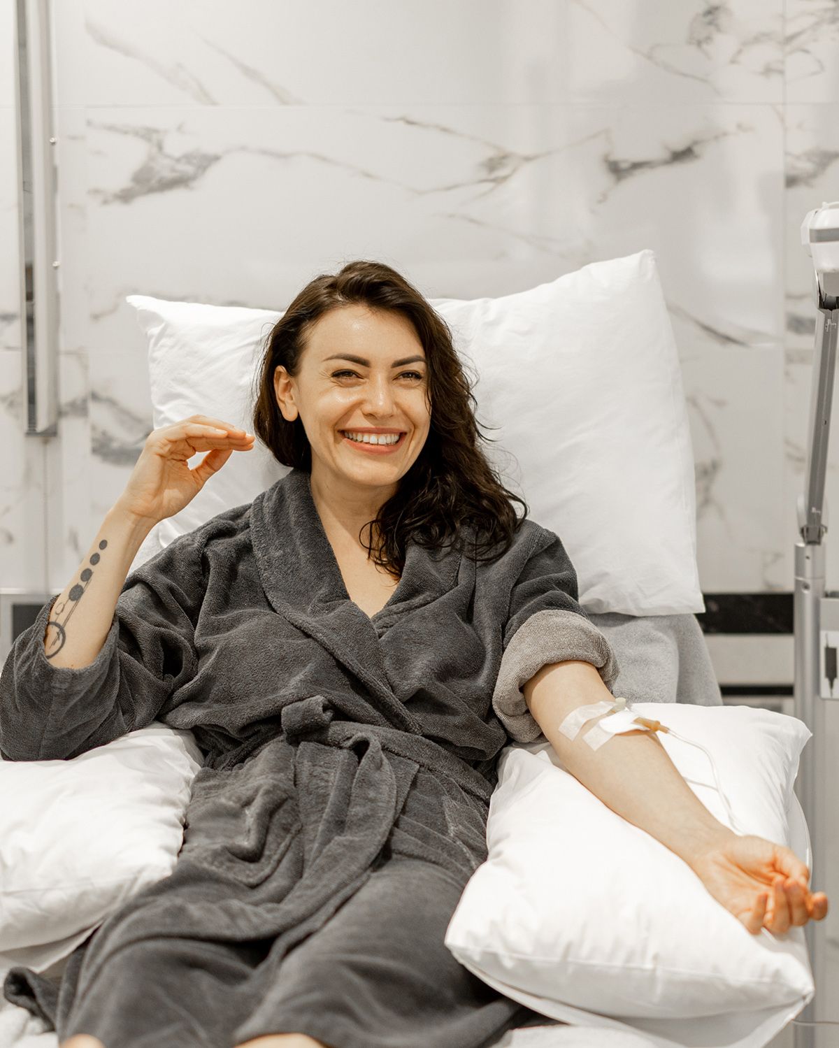 Smiling patient reclining in a hospital chair, receiving an IV and wrapped in a gray robe