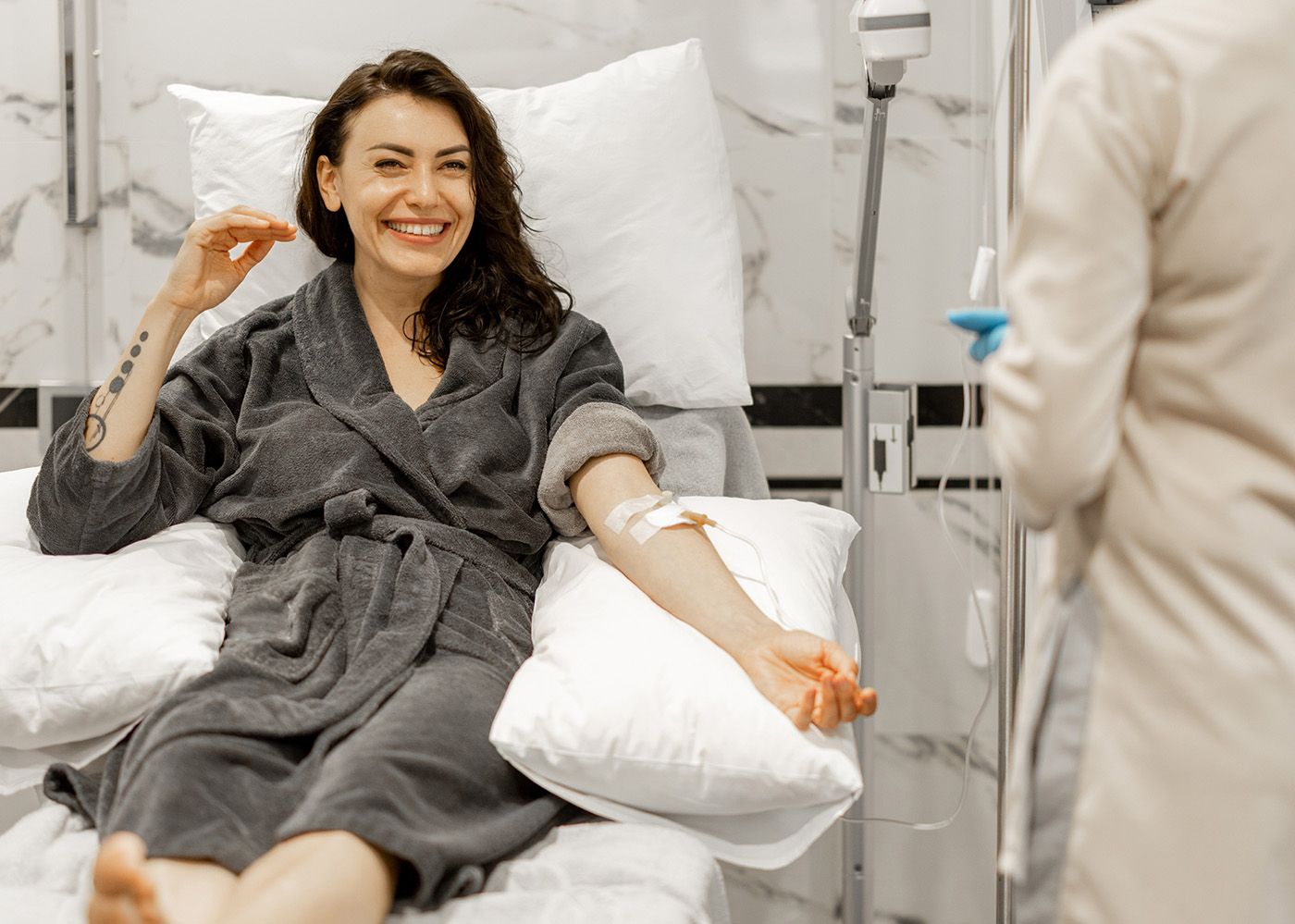 Smiling patient in a gray robe receives an arm injection in a clinic