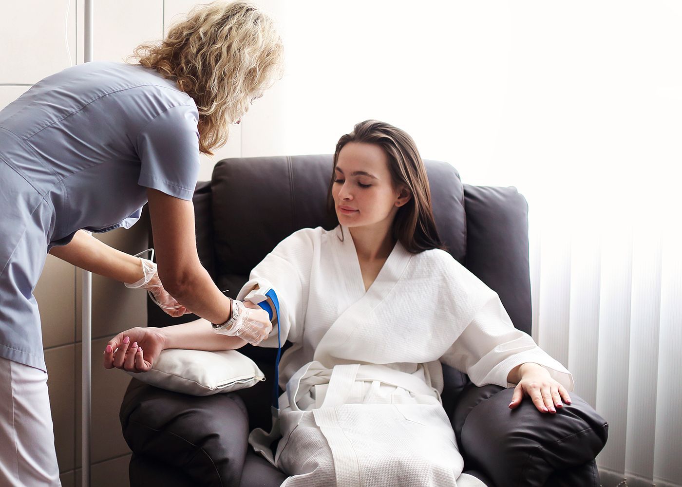 Caregiver bandages a seated patient’s arm in a bright living room.