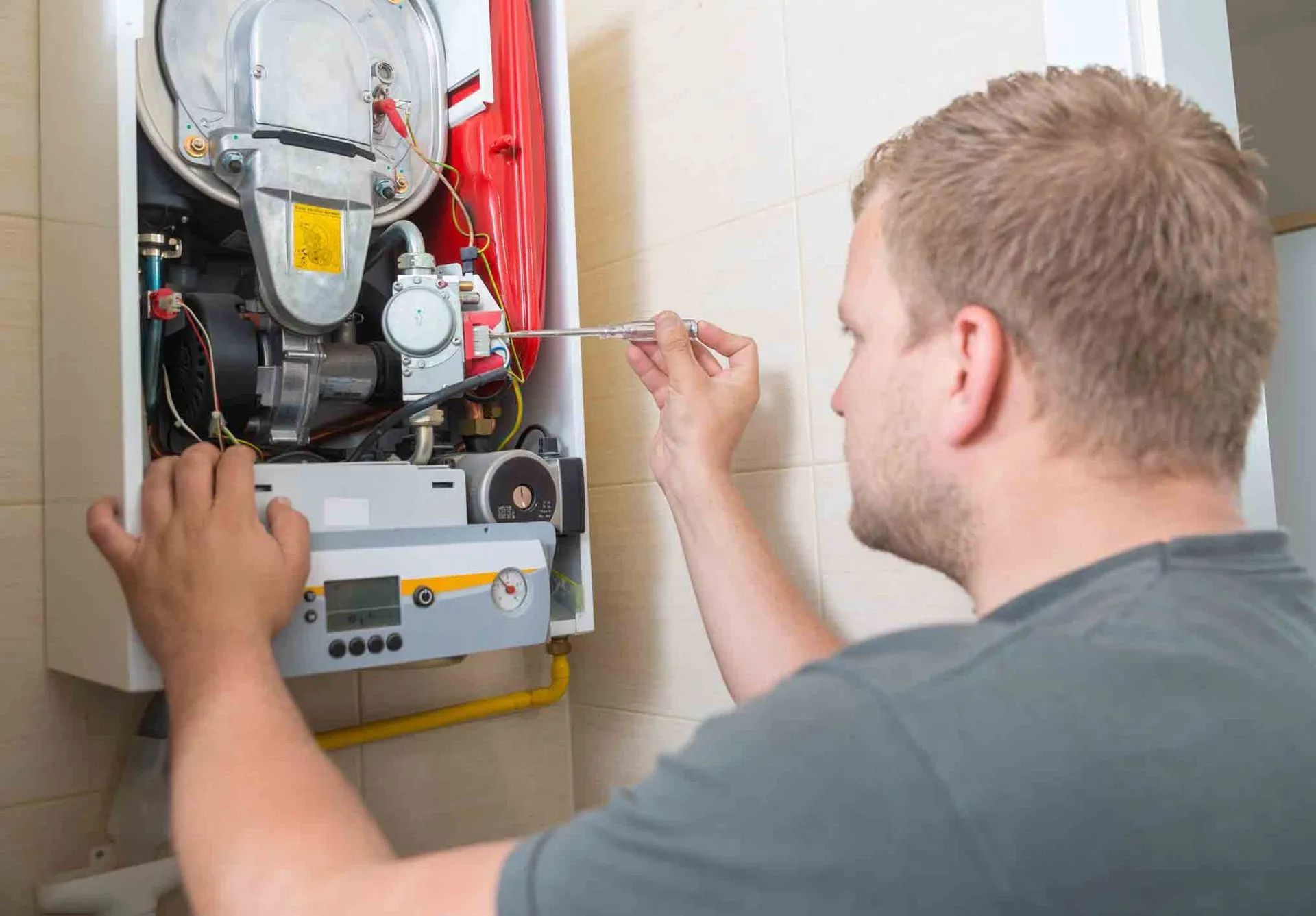 A man is fixing a boiler with a screwdriver.