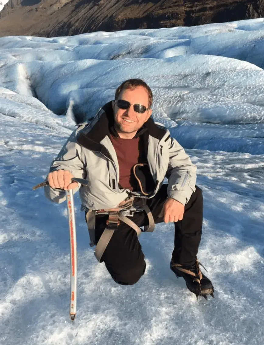 A man is kneeling down in the snow holding a pole.