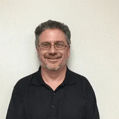 A man wearing glasses and a black shirt is smiling for the camera.